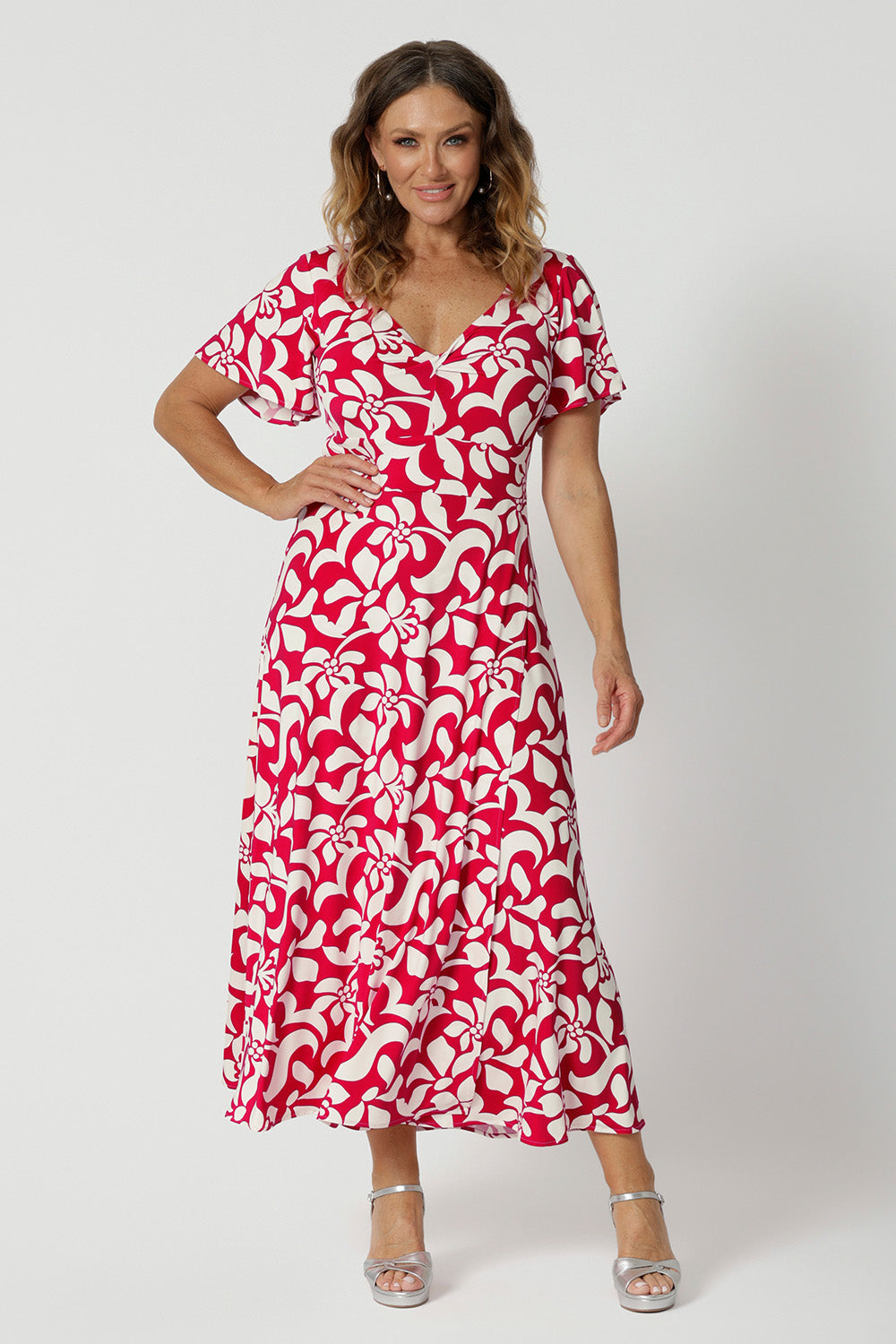 Over 40 year old woman's wears red and ivory coloured maxi floral dress. Dress for summer has a twist front bodice and flutter sleeves. Floral fabric used is easy-care and crease-resistant perfect for travel and easy packing. Leina & Fleur is a woman's clothing brand that actively stocks sizes from 8-24. Shop this summer ready dress in petite sizes and plus sizes.