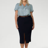 Full body front view of 40 year old plus sized woman wearing a midi length work skirt. This workwear skirt is navy in colour and made of good quality scuba crepe fabric. This skirt has an above the knee slit for comfort and mobility. Perfect skirt for an office or corporate setting. 3/4 length skirt is Australia made by New Zealand and Australian women. Leina & Fleur is a clothing company for woman that stock sizes from 8 to 24. Shop this work skirt in plus sizes and petite sizes. 
