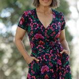 Featuring a striking floral print in bold shades of pink, green, burgundy, and blue, this dress flatters with its true wrap silhouette, extended waist ties, and a flowing A-line skirt.