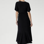 Black jersey wrap dress with extended waist ties, sweetheart neckline, and feminine flutter sleeves — perfect for events and celebrations.