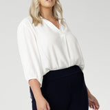 Plus size woman wears Vanilla workwear shirt. A soft tailored shirt with 3/4 sleeves, collar neckline and shirttail hem. Pull on style shirt is made in Australia from sustainable Tencel fabric. Easy care workwear blouse for women, available in 8-24.