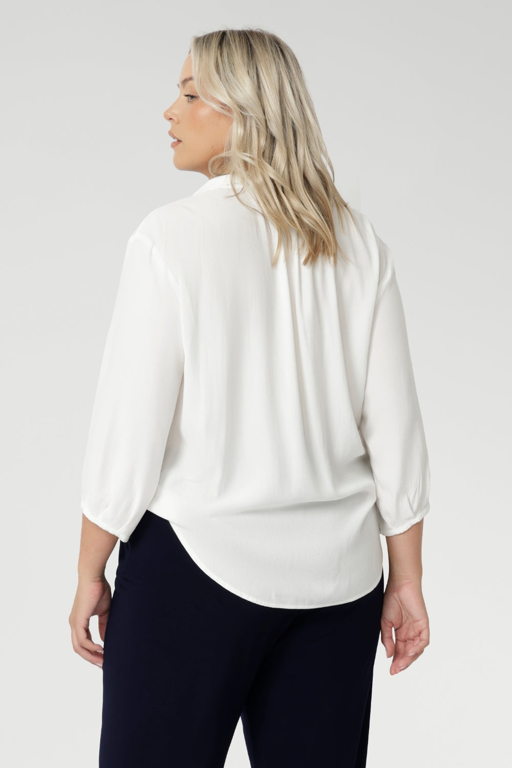 Back view image of size 18 woman wearing the Arley Shirt in in Vanilla. A soft tailored shirt with 3/4 sleeves, collar neckline and shirttail hem. Pull on shirt is made in Australia of sustainable tencel fabric. Soft and easy care workwear for women for petite to plus size 8-24. Styled back with a Bradley culotte in navy. 