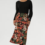 Designed with a modern, feminine cut, it features a boat neckline and full-length bellow sleeves. Size 10 woman wears her Knit Top with a floral printed skirt.