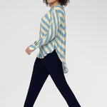 The Blue Sky Stripe blends soft sky blue and vanilla tones. Made in Australia. Women wears stripe blouse with tapered leg work pants in navy. 