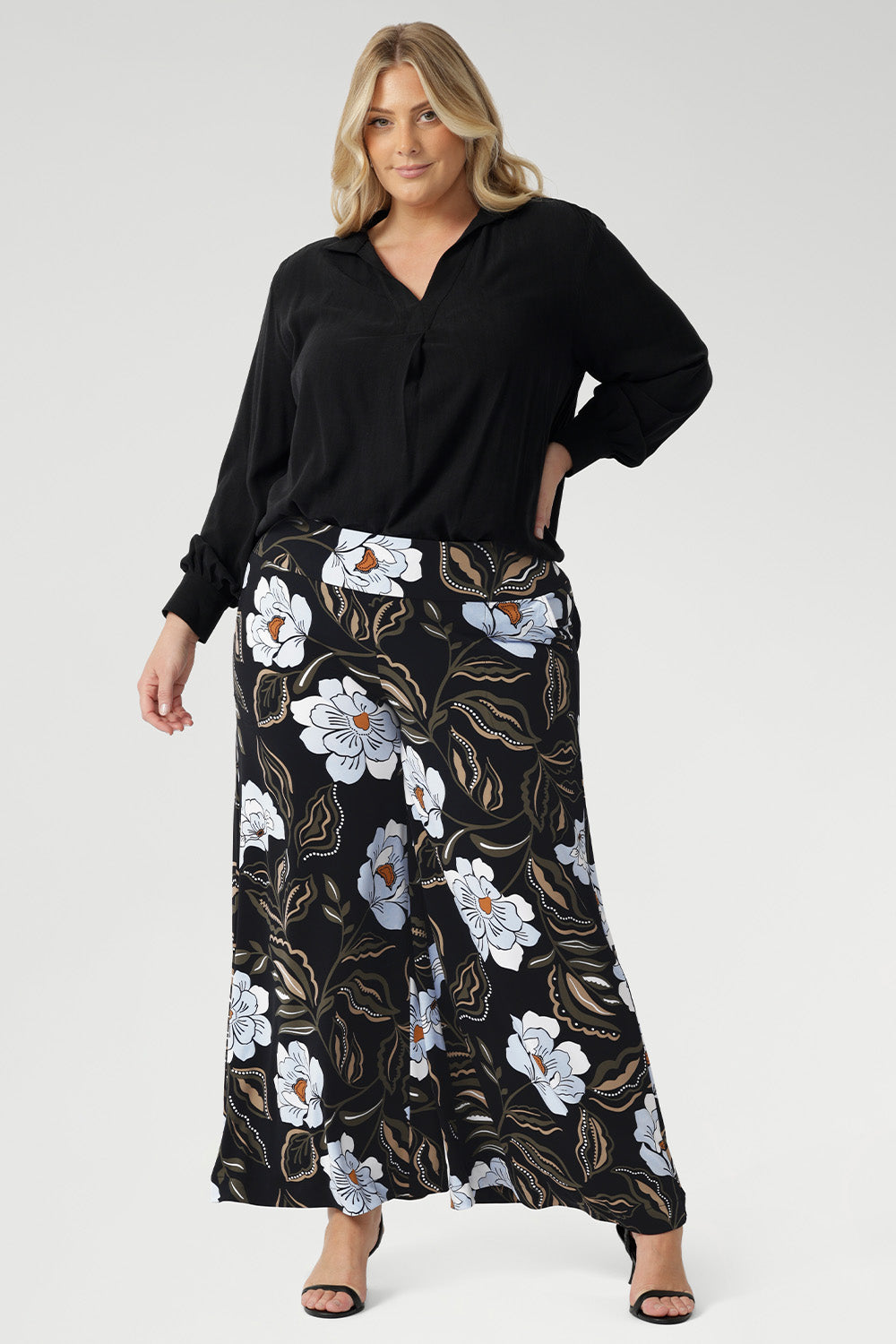 Plus size woman wears the Ellis shirt in Graphite Black styled tucked into printed wide leg pants and black heels for an elevated stylish. 