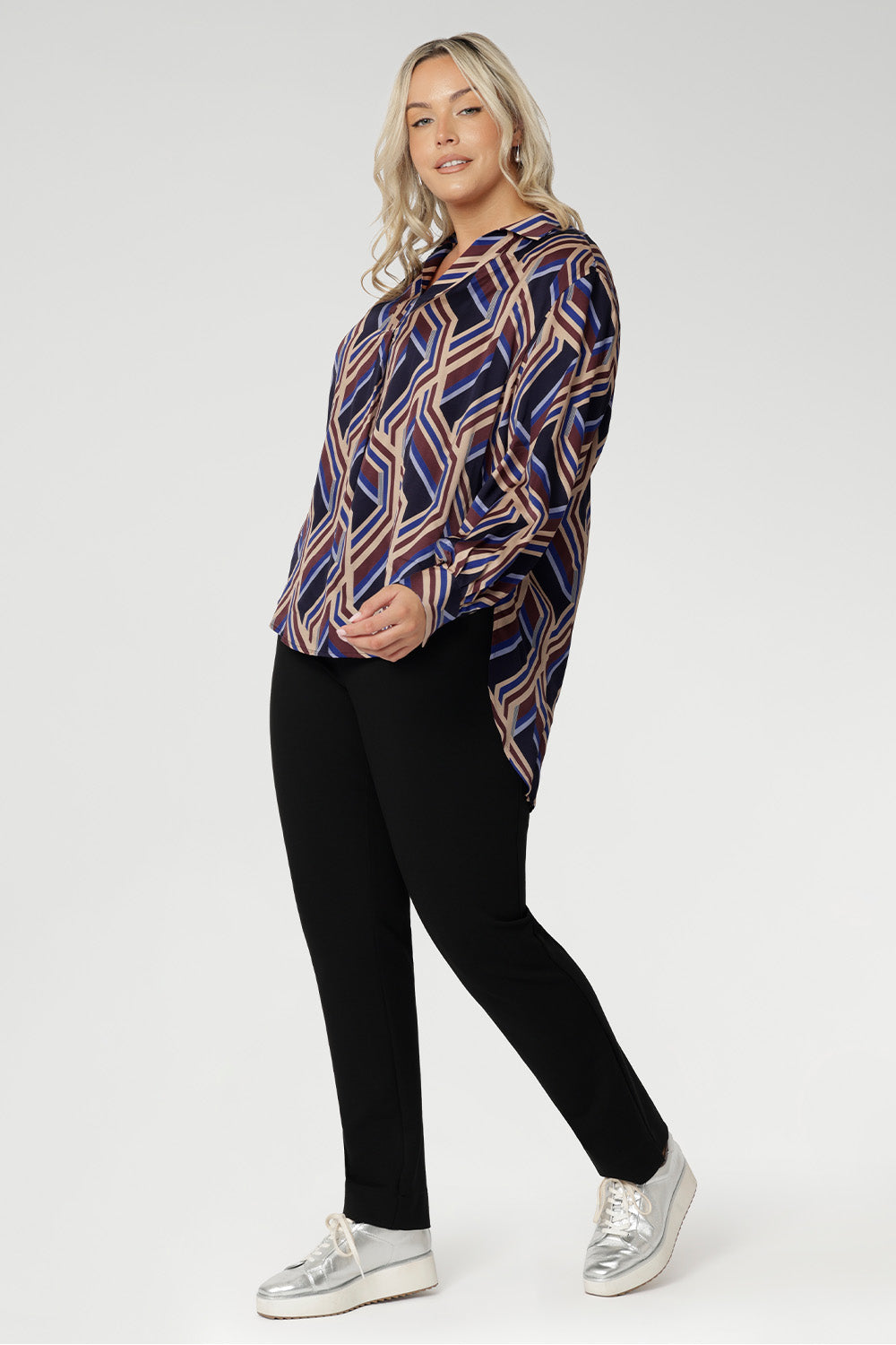 The Ellis Shirt is a versatile, statement-making piece perfect for work, weekends, or layering under jackets throughout the season. Plus size model wears geometric shirt with black work pants. 