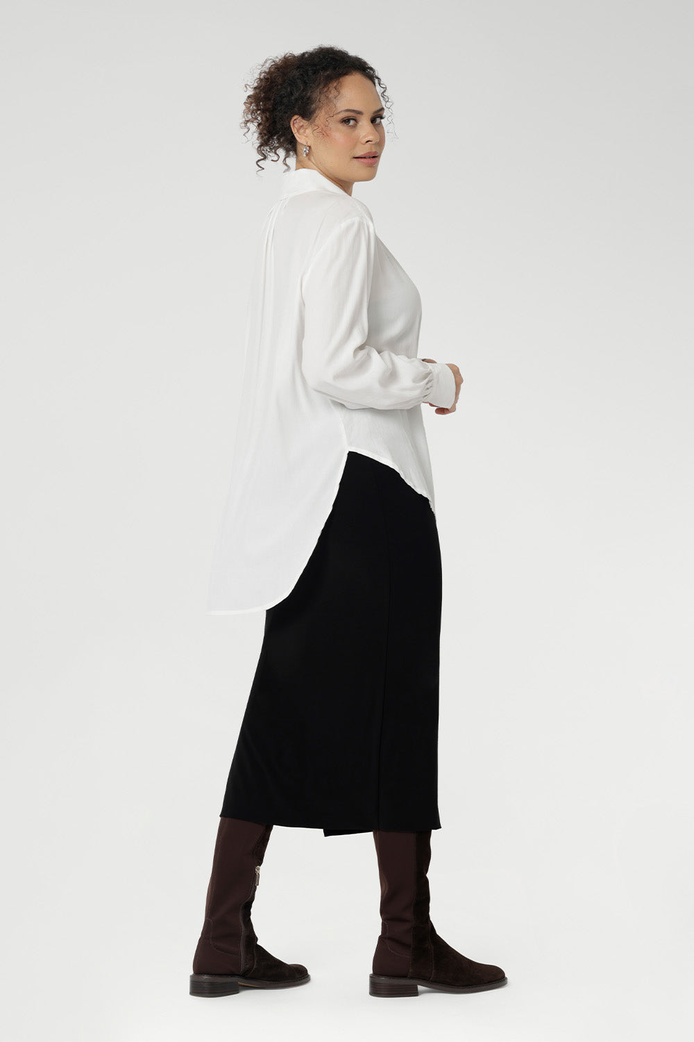 Back view of a size 10 woman wears the Ellis shirt in Vanilla tencel, a high quality made in Australia womens shirt made in breathable tencel. Inclusive size range 8-24 and made in Australia. Styled with black midi tube skirt and brown boots. 