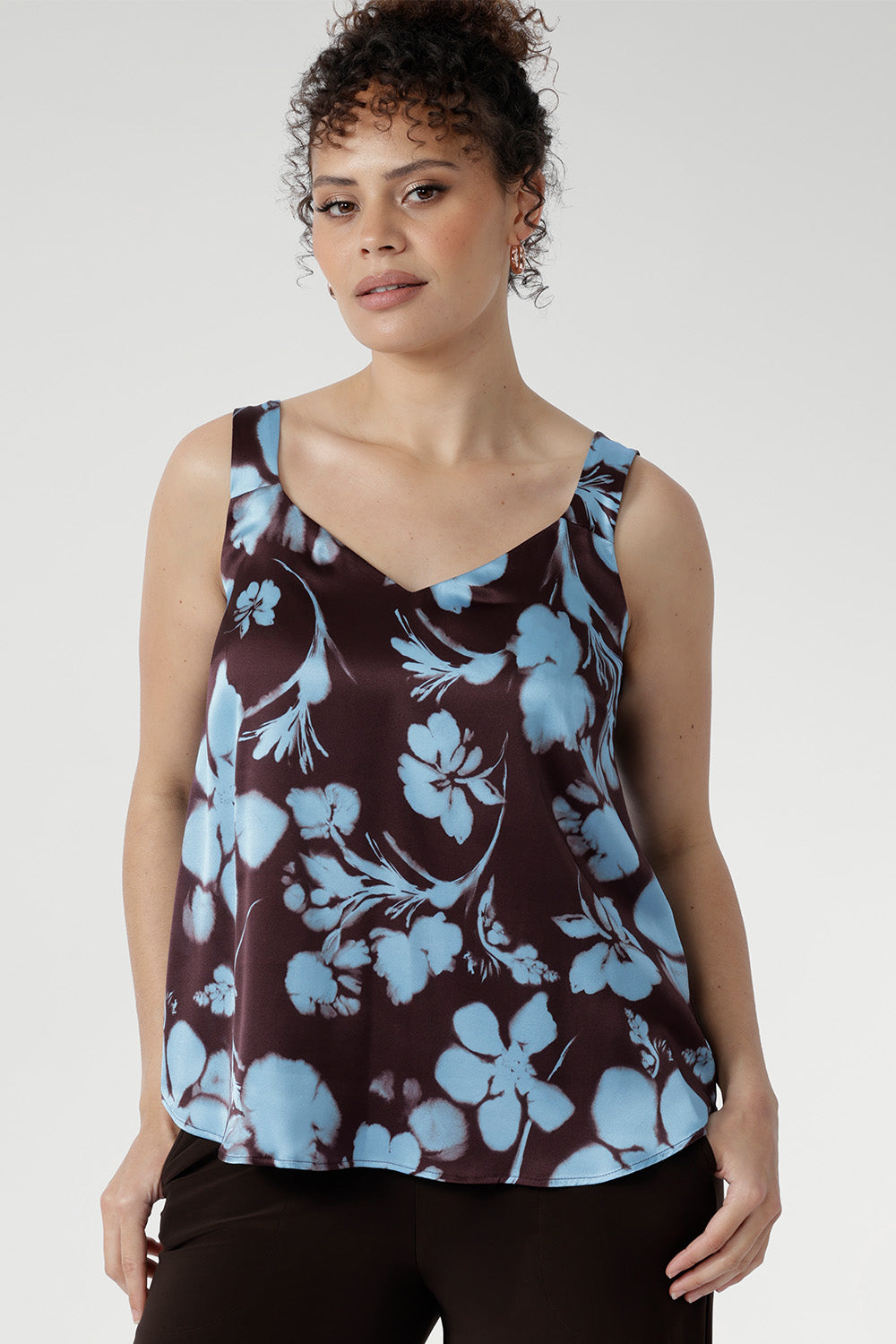 Woman wearing a sleeveless top with blue floral pattern on a plain background