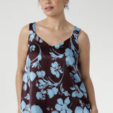 Woman wearing a sleeveless top with blue floral pattern on a plain background
