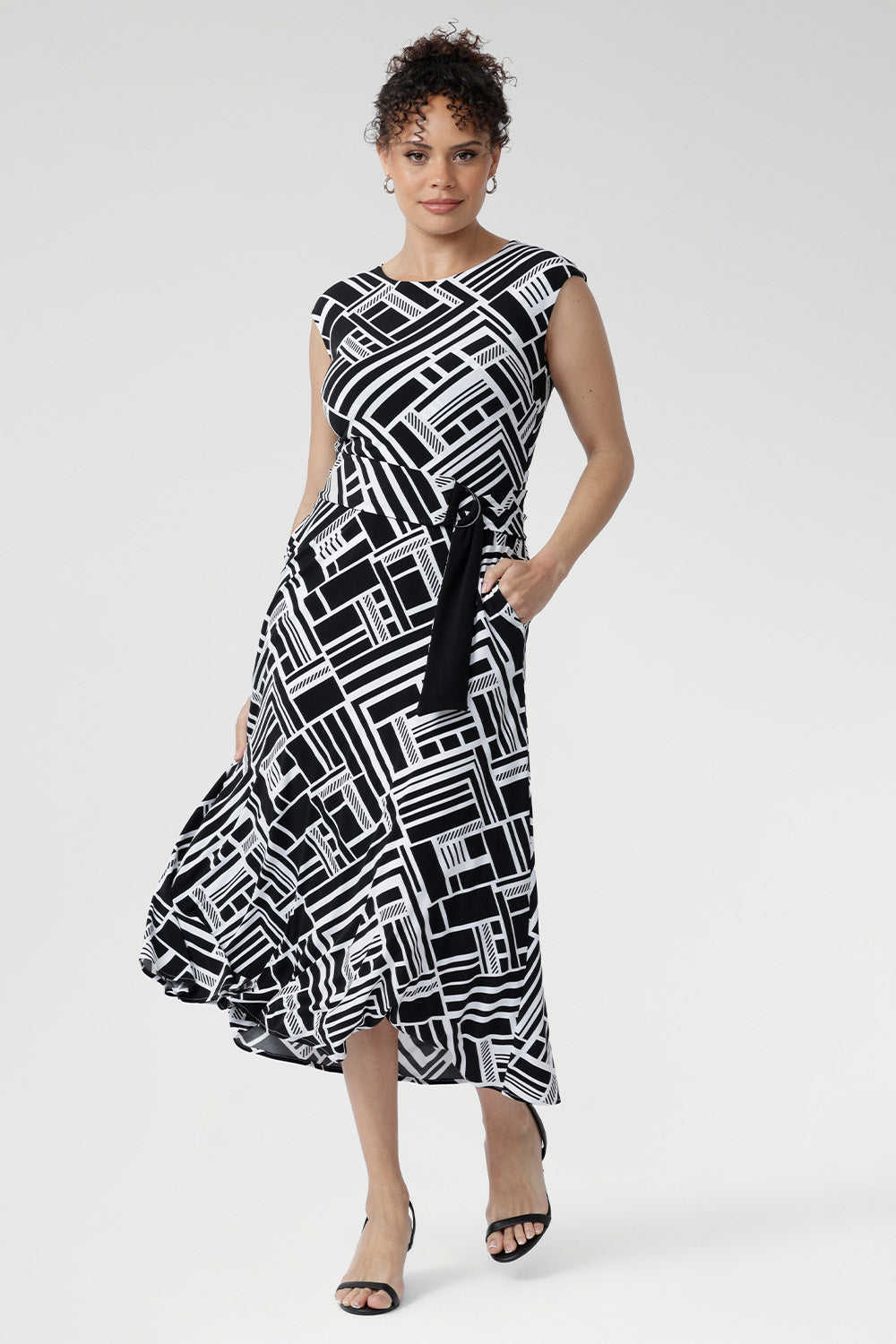 Size 10 woman wearing a black and white geometric patterned dress with matching belt and black kitten heels.