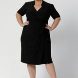 Size 18 woman wears the Kriss dress in black. A functioning wrap work dress in soft black jersey. Great for being comfortable in the office. Made in Australia for women size inclusive fashion 8 - 24.