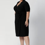 A size 18 woman wears the Kris dress in black. A functioning wrap work dress in soft black jersey. Great for being comfortable in the office. Made in Australia for women size inclusive fashion 8 - 24.