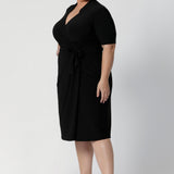 A size 18 woman wears the Kris dress in black. A functioning wrap work dress in soft black jersey. Great for being comfortable in the office. Made in Australia for women size inclusive fashion 8 - 24.