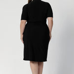 Back view of a size 18 woman wears the Kris dress in black. A functioning wrap work dress in soft black jersey. Great for being comfortable in the office. Made in Australia for women size inclusive fashion 8 - 24.