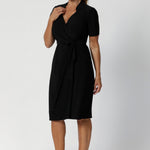 A size 12 woman wears the Kris dress in black. A functioning wrap work dress in soft black jersey. Great for being comfortable in the office. Made in Australia for women size inclusive fashion 8 - 24.