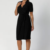 A size 12 woman wears the Kris dress in black. A functioning wrap work dress in soft black jersey. Great for being comfortable in the office. Made in Australia for women size inclusive fashion 8 - 24.