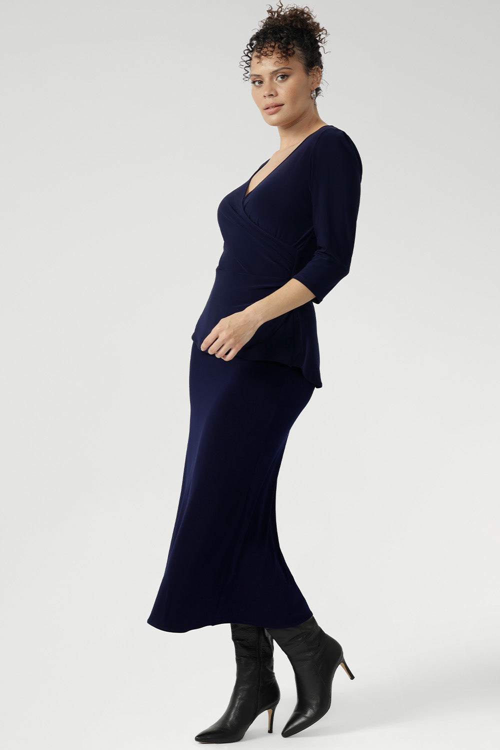 Whether you're in the office or heading to after-work events, the Kyle Top delivers confidence and style with ease. Size 10 model wears navy wrap top with navy midi  skirt and black boots for a faux dress look.