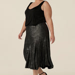 Side view of a size 18, plus size woman wears a midi length, foil print evening skirt with ruffle hem. For cocktail and evening wear, this elegant skirt is worn with a black cami top. Both cocktail skirt and top are made in Australia by women's fashion brand, Leina & Fleur. Shop their evening and cocktail wear online in petite to plus sizes.