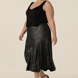 Side view of a size 18, plus size woman wears a midi length, foil print evening skirt with ruffle hem. For cocktail and evening wear, this elegant skirt is worn with a black cami top. Both cocktail skirt and top are made in Australia by women's fashion brand, Leina & Fleur. Shop their evening and cocktail wear online in petite to plus sizes.