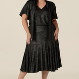 A size 18, plus size woman wears a midi length, foil print evening skirt with ruffle hem. For cocktail and evening wear, this elegant skirt is worn with a foil print top with flutter sleeves and neck ties to create a faux cocktail dress. Both cocktail skirt and top are made in Australia by women's fashion brand, Leina & Fleur. Shop their evening and cocktail wear online in petite to plus sizes.