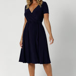 A curvy, size 12 woman wearing a navy, wrap dress with short sleeves. A great dress for summer casual wear, or for back to work. Shop made in Australia dresses in petite to plus sizes online at  fashion brand, Leina & Fleur. Shop Maree Dress in Navy in sizes 8-24.
