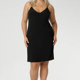 A size 18 woman wears a mini-length, reversible slip in black jersey fabric. The slip has thin straps and is worn with a V neck to the front. Made in Australia to layer under dresses and separates. Plus size slip dress for women. Available in size 8-24.