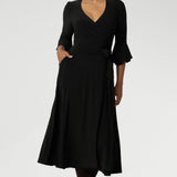 Size 10 corporate woman wears the Portia dress in Black. A wrap dress in black with tie side and 3/4 sleeve. Styled with long brown boots. Made in Australia for women size 8 - 24.