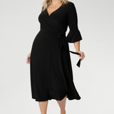Size 18 corporate woman wears the Portia dress in Black. A midi length wrap dress in black with a side tie and 3/4 sleeve. Made in Australia for women size 8 - 24.