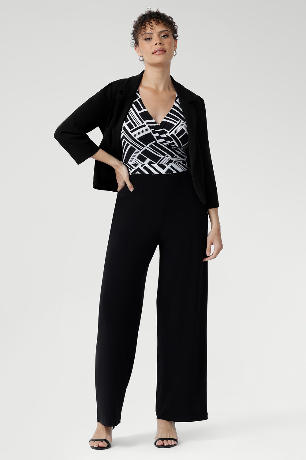 The Puzzle Jumpsuit transitions seamlessly from workwear to evening outings, making it the ultimate wardrobe multitasker Size 10 woman wears her black and white playsuit with Merit Blazer in Black 