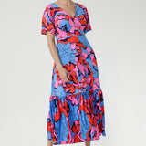 Crafted from slinky jersey, the Rio Dress in Can Can is a lightweight maxi featuring a flattering empire-line bodice, deep V-back, flared sleeves, and a gathered hem with a flowing tail effect—perfect for effortless summer elegance.