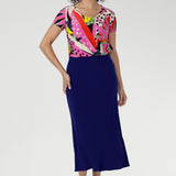 The Tucan print blends abstract strokes of pinks, reds, greens, and black on a warm cream base, creating a vibrant, artful pop that enlivens any outfit. Size 10 woman wears her Sawyer top with a cobalt colour skirt to make the print pop.
