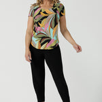 A size 10 woman wears the Sawyer Top in jersey with Zanzibar print. A multi coloured print with a black base and beautiful bright colours. Made in Australia for women size 8-24. Styled back with the Indi Pant in Black.  
