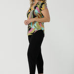A size 10 woman wears the Sawyer Top in jersey with Zanzibar print. A multi coloured print with a black base and beautiful bright colours. Made in Australia for women size 8-24. Styled back with the Indi Pant in Black.  