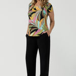 A size 10 woman wears the Sawyer Top in jersey with Zanzibar print. A multi coloured print with a black base and beautiful bright colours. Made in Australia for women size 8-24. Styled back with the Monroe Pant in Black.  